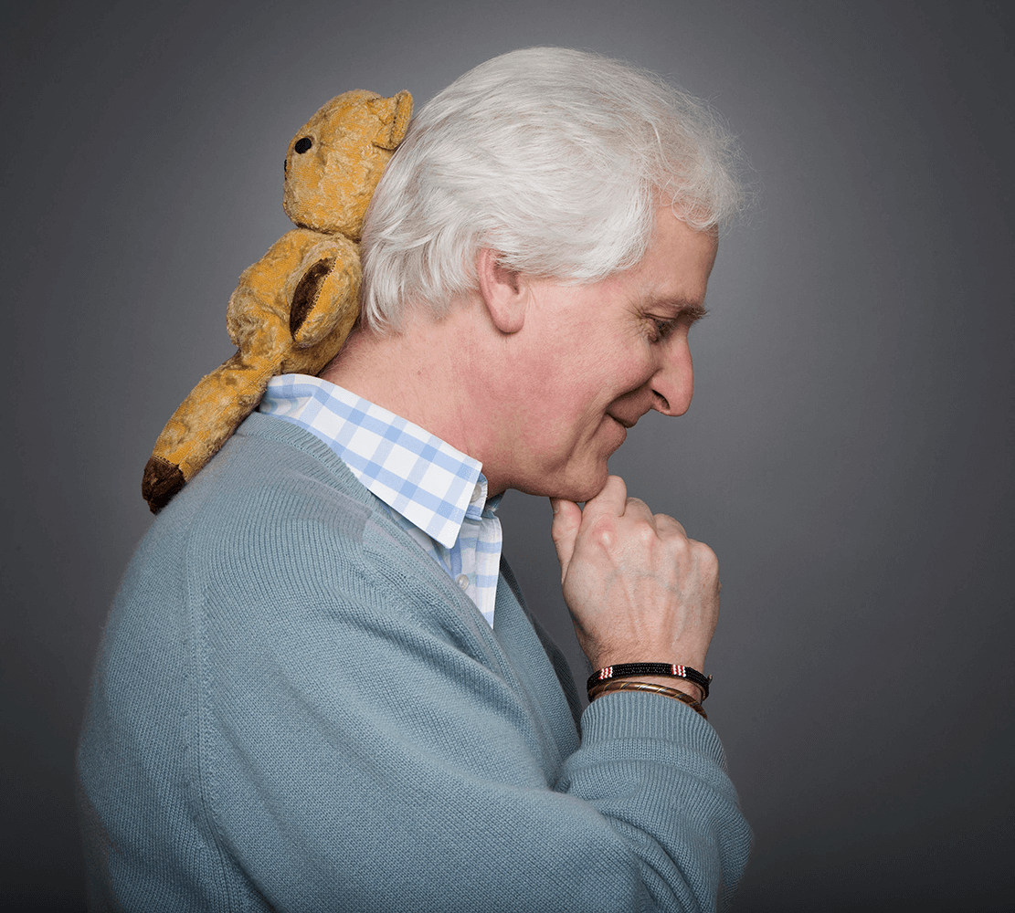 Headshot of Child Psychotherapist Julian Tomkins side profile with an old, well-loved teddy bear on his back.