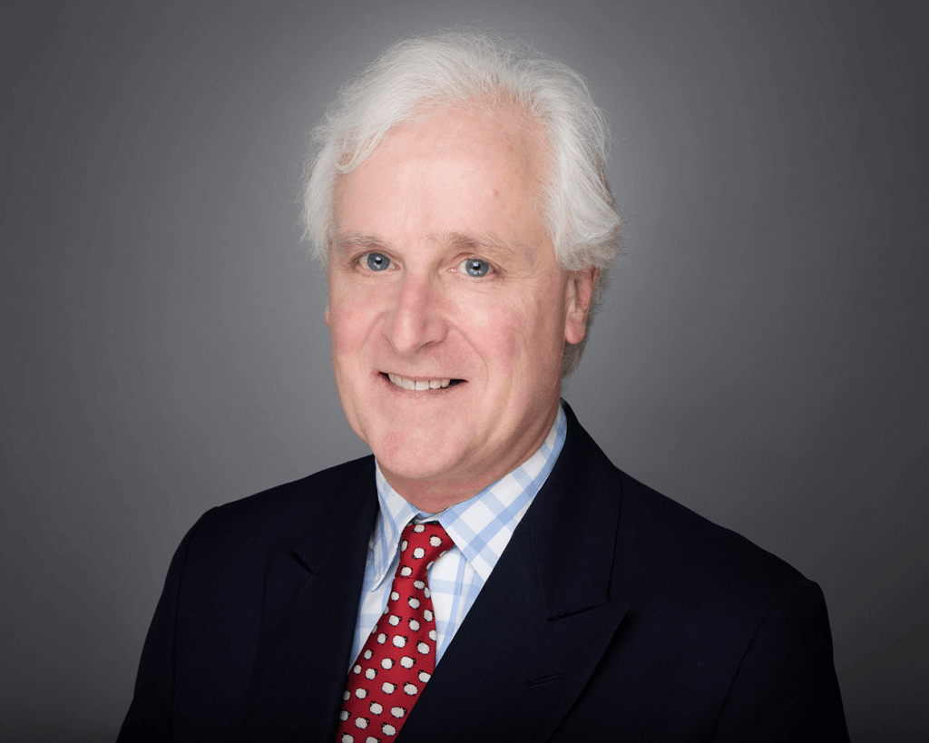 Headshot of Therapeutic Counsellor Julian Tomkins wearing a black suit with a red sheep tie and smiling.
